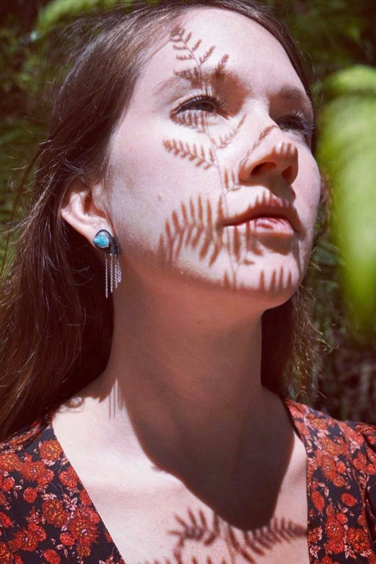 Woman with a ferm shadow on her face face wearing sky swell earrings against a natural background
