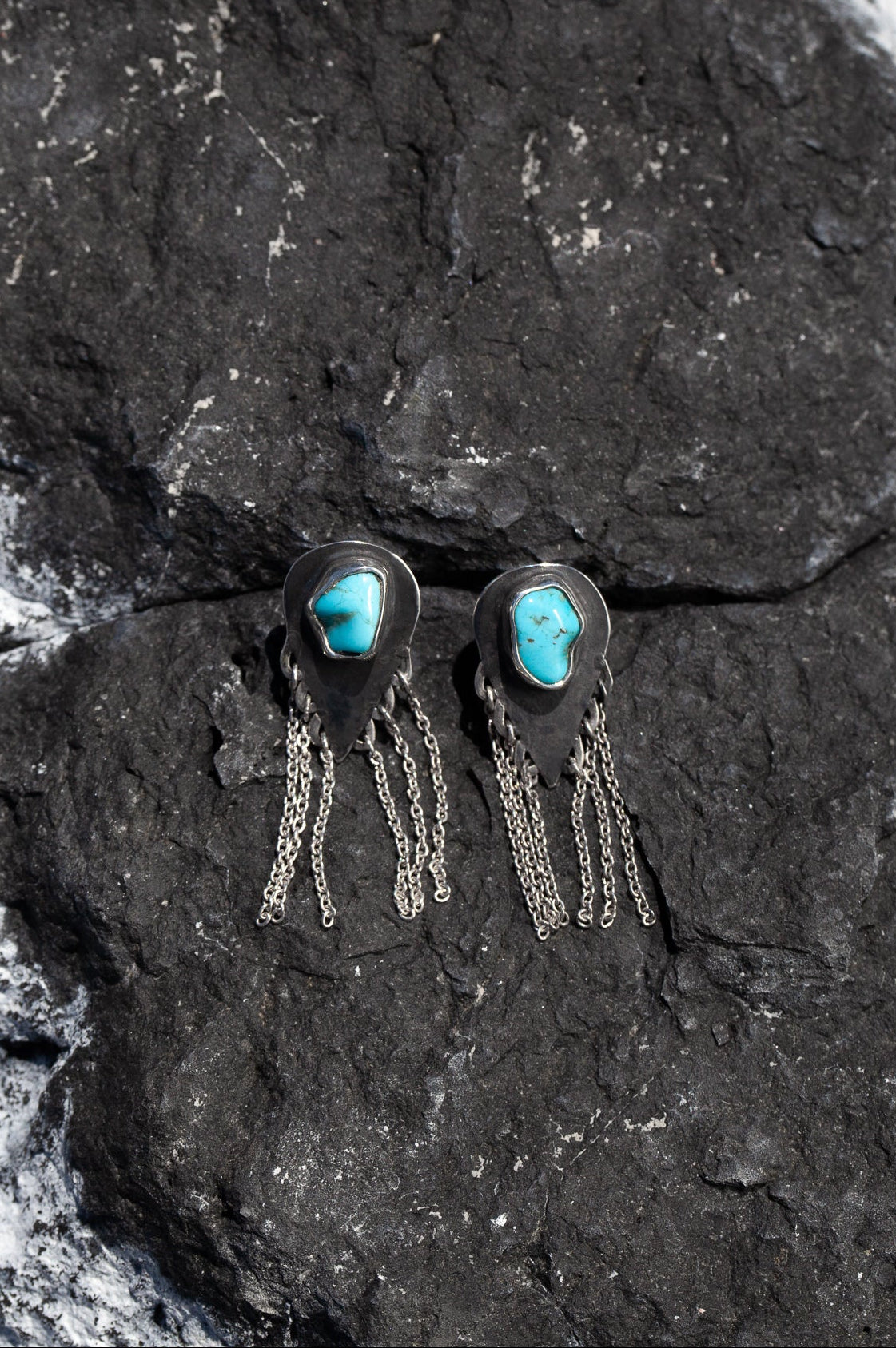 Pair of silver earrings with turquoise stones with delicate chain dangles on a dark stone surface